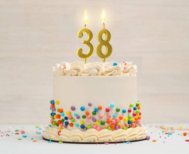 Yanan mumlar ve hafif arka planda serpiştirilmiş mumlarla nefis bir pasta. 38. yaş günü veya diğer özel günler