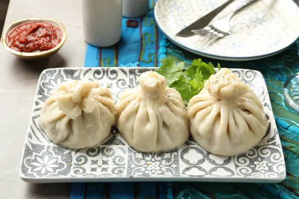 Gri masada soslu kişniş ve kişniş ile servis edilen lezzetli khinkali, yakın plan.