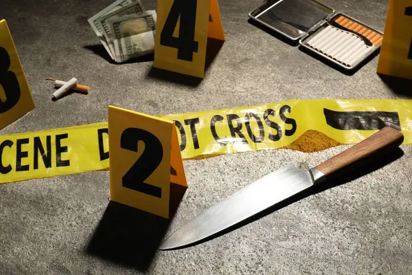 Adli tıp uzmanlığı. Gri arka planda delil, işaret ve polis bandı olan olay yeri, yakın plan.