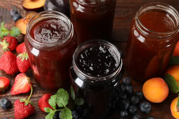 Kavanozlardaki farklı reçeller ve ahşap masadaki malzemeler, yakın plan.