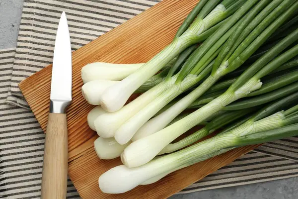 Taze taze taze soğanlar kesme tahtası ve bıçakla gri masada, düz yatıyordu.