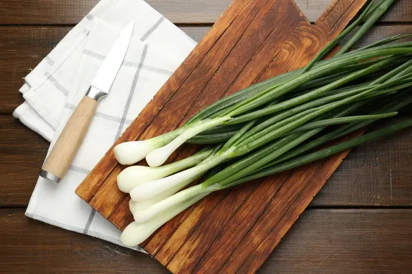 Taze taze soğanlar, tahta kesme tahtası ve bıçakla tahta masada, düz yatıyordu.