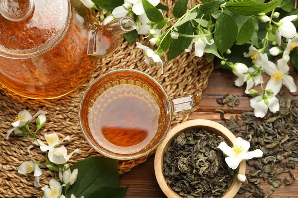 Aromatik yasemin çayı cam fincanda, çaydanlıkta, demlikte ve çiçeklerde ahşap masada, düz yerde.