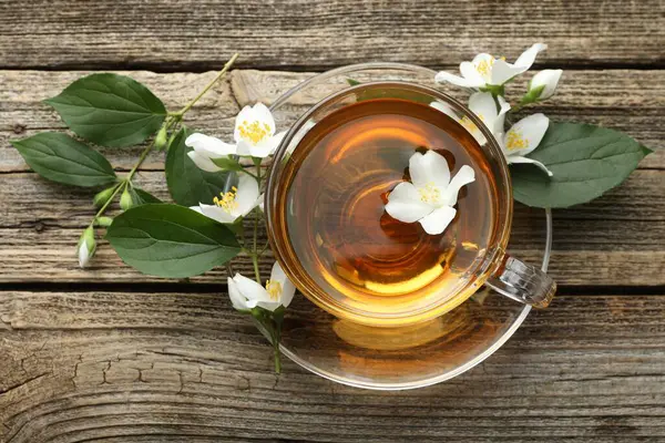 Cam bardakta Aromatik yasemin çayı, tahta masada çiçekler ve yeşil yapraklar, düz uzanmış