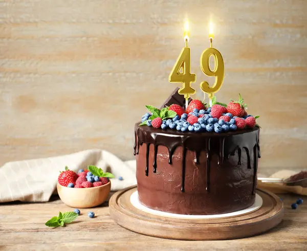 Böğürtlenli çikolatalı kek ve ahşap masada yanan mumlar. Mesaj için yer var. 49. yaş günü veya diğer özel günler