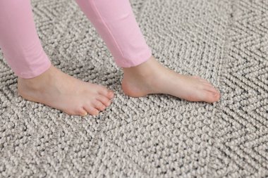 Evdeki gri halıda yürüyen kız, yakın plan.