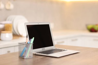 Boş ekranlı dizüstü bilgisayar ve mutfaktaki ahşap masada kırtasiye malzemesi, seçici odaklanma. Tasarım için model