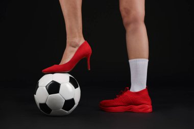 Arka planda futbol topu olan yüksek topuklu ayakkabılı ve spor ayakkabılı bir kadın.