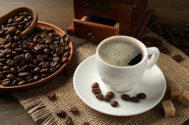 Aromatik kahve fincanda, fasulye, esmer şeker ve öğütücü ahşap masada, yakın plan.