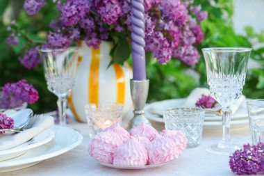 Güzel leylak çiçekleri, zephyrler, tabaklar, çatal bıçaklar, bardaklar ve mumlar bahçede, yakın plan