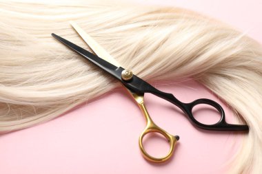 Açık pembe arka planda saç teli ve makas, yakın plan.