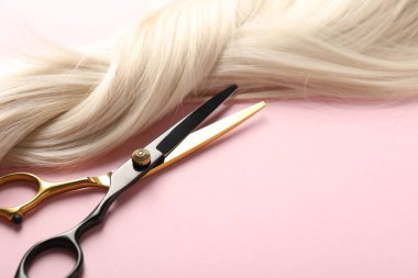 Açık pembe arka planda saç teli ve makas, yakın plan. Metin için boşluk
