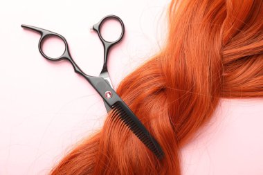 Açık pembe zemin üzerinde saç teli ve makas, üst görünüm