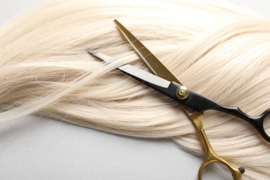 Açık gri arkaplanda sarı saç tokası ve makas, üst görünümde.