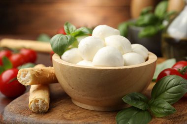 Lezzetli mozzarella peynir topları, ekmek çubukları, domates ve fesleğen ahşap masada, yakın plan.