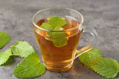 Cam bardakta Aromatik limon merhemi çayı ve gri desenli masada taze yapraklar, yakın plan.
