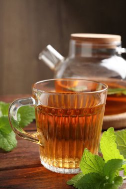 Cam fincanda aromatik limon merhemi çayı, çaydanlık ve ahşap masada taze yapraklar, yakın plan.