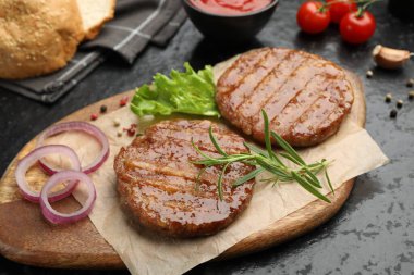 Lezzetli hamburger köfteleri, domatesler ve baharatlar siyah masada, yakın plan.