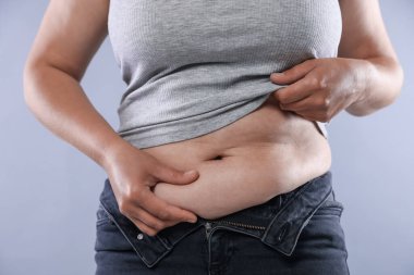 Hafif arka planda aşırı göbek yağı olan kadın, yakın plan. Aşırı kilolu