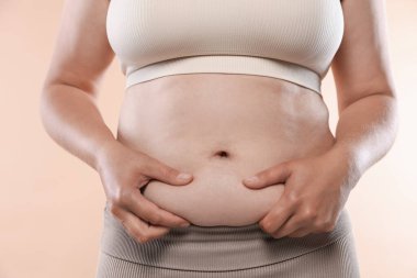 Bej arka planda aşırı göbek yağlı bir kadın, yakın plan. Aşırı kilolu