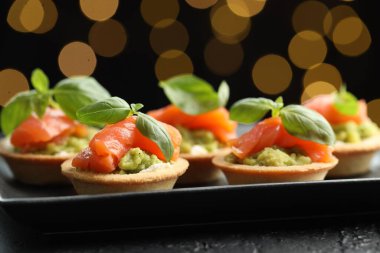 Siyah masadaki lezzetli kanepeler karanlık arka planda bulanık ışıklarla, yakın plan. Bokeh etkisi