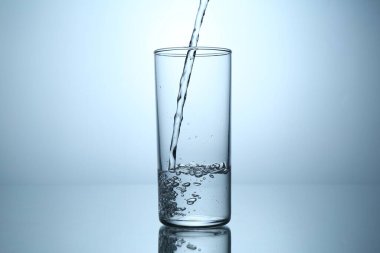 Ayna masasında açık gri gradyan arkaplana karşı cama su dökmek, yakın plan