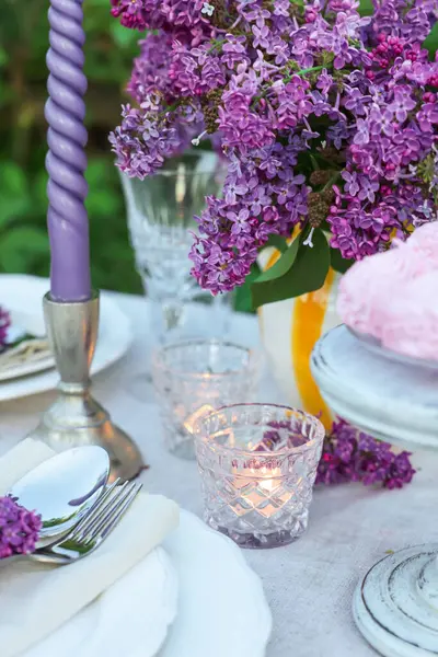 Güzel leylak çiçekleri, tabaklar, çatal bıçak takımı ve yanan mumlar bahçede, yakın plan.