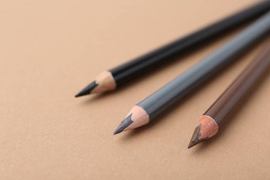 Bej arka planda üç farklı kaş kalemi, yakın plan. Metin için boşluk