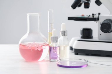 Lüks parfüm yapıyorum. Temel yağlar cam eşyalar, çiçekler ve mikroskop beyaz ahşap masa üzerinde, yakın çekim