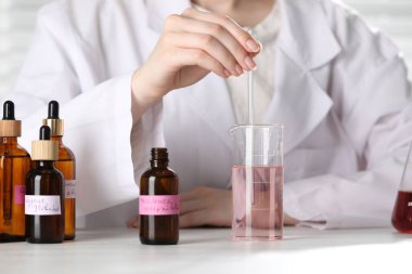 Laboratuvarda beyaz ahşap masada lüks parfüm üreten profesyonel bir parfümcü.