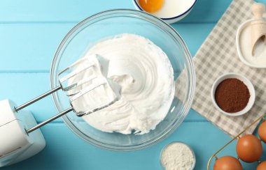 Krem şantili kase, el mikseri ve malzemeler açık mavi ahşap masa, düz yatıyordu.