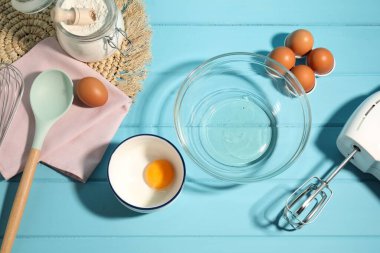 Krem şanti yapıyorum. Kase, el çırpıcı ve malzemeler açık mavi ahşap masada, düz yerde.