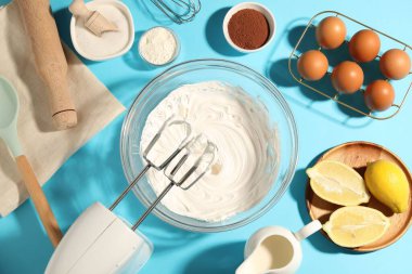 Açık mavi masada çırpılmış krema, yumurta ve diğer ürünlerle el çırpıcı, düz konum