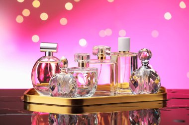 Ayna yüzeyinde birçok farklı parfüm şişesi var. Pembe arka planda bulanık ışıklar, yakın plan.