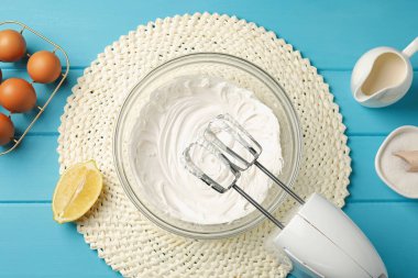 Açık mavi ahşap masa üzerinde çırpılmış krema, yumurta ve diğer ürünlerle el çırpıcı düz yatıyordu.