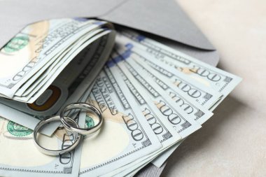 İki gümüş alyans, bir dolarlık banknotlar ve beyaz masanın üzerindeki zarf, yakın plan.