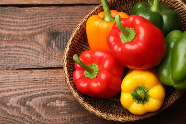 Hasır sepetin içinde taze renkli dolmalık biberler, ahşap masa, üst manzara. Metin için boşluk