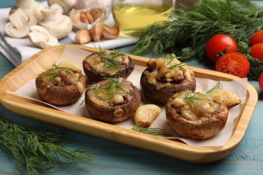 Eritilmiş peynirli, sarımsaklı ve dereotlu leziz mantarlar açık mavi ahşap masada, yakın plan.