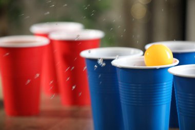 Bira pong oyunu. İçkili plastik bardaklar ve tahta masanın üzerinde top, yakın plan. Metin için boşluk