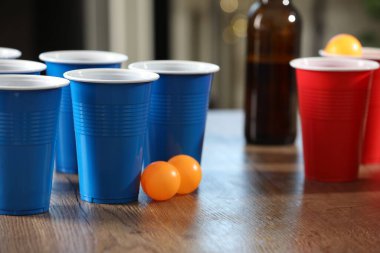 Bira pong oyunu. İçkili plastik bardaklar ve toplar ahşap masada, yakın plan.