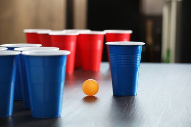 Bira pong oyunu. İçkili plastik bardaklar ve tahta masada top, yakın plan.