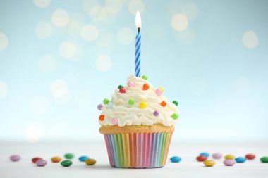 Kekin içinde yanan mum ve masasında mavi arka planda bulanık ışıklarla duran şekerler.