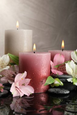 Yanan mumlar, kaplıca taşları ve ıslak siyah masada güzel çiçekler, yakın plan.