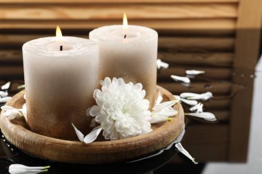 Islak siyah ayna yüzeyinde yanan mumlar ve güzel çiçekler, yakın plan.