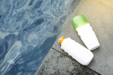 Dışarıdaki yüzme havuzunun yakınındaki taş yüzeyde bulunan güneş koruma ürünleri şişeleri.