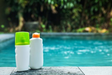 Dışarıdaki yüzme havuzunun yakınındaki taş yüzeyde güneş koruma ürünleri şişeleri, metin için yer.