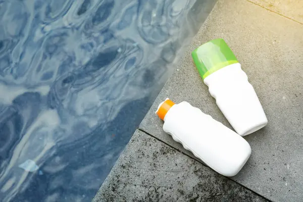 Dışarıdaki yüzme havuzunun yakınındaki taş yüzeyde bulunan güneş koruma ürünleri şişeleri.