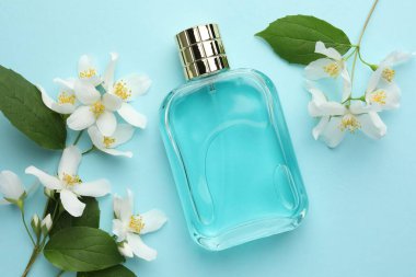 Bir şişe parfüm, güzel yasemin çiçekleri ve açık mavi arka planda yeşil yapraklar.