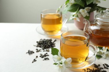 Camdan fincanlar, çaydanlık, çiçekler ve beyaz masanın üzerindeki kurumuş yapraklar içinde yasemin çayı, yakın plan. Metin için boşluk