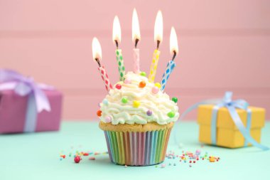 Kekin içinde mum yakmak, serpiştirmek ve pembe arka planda turkuaz masa üzerinde hediye kutuları.